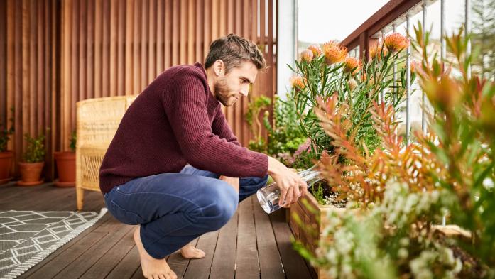 Young man giving water to plants in the balcony of his house