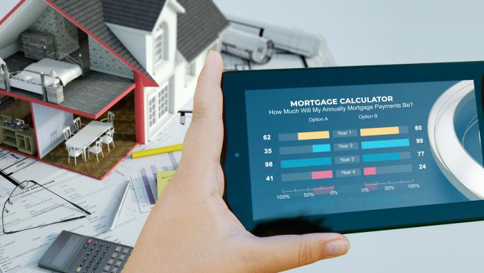 hands holding a phone displaying mortgage calculator with small model home over papers in background