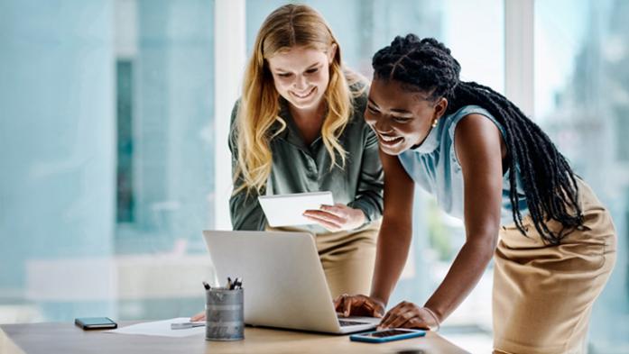 Two businesswomen working together on a digital tablet and laptop in an office