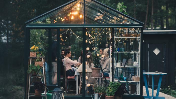 Young multi-ethnic friends enjoying dinner party in glass conservatory room at back yard 