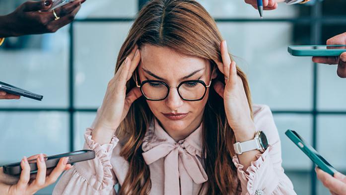 Photo of a stressed woman with hands holding many types of tech out to her