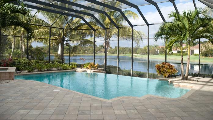 A backyard pool located in a tropical setting covered by a screen lanai. Lake in behind.