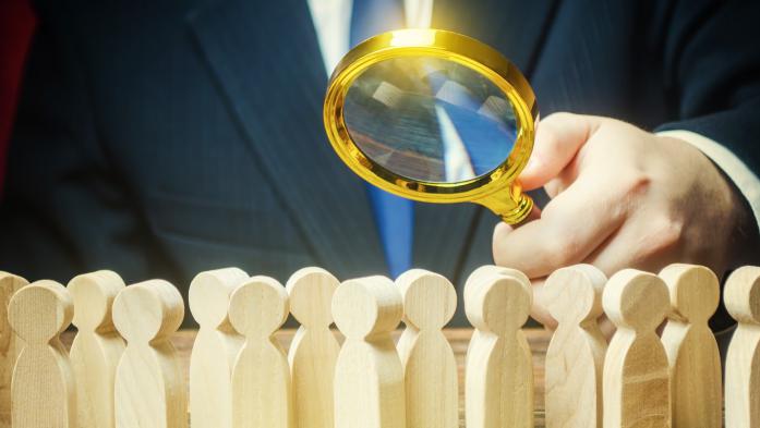 hand holding a magnifying glass over a group of wooden block people