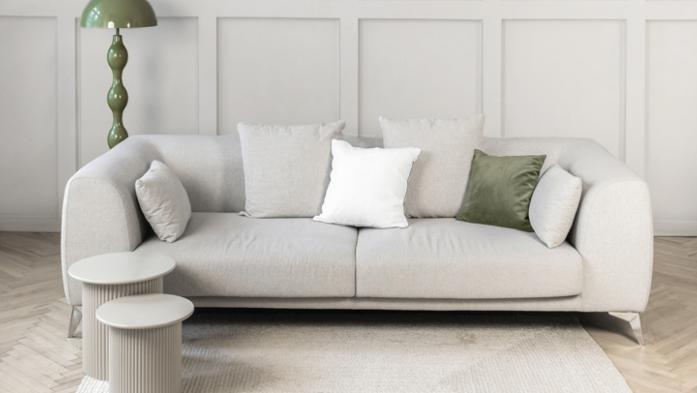 Stylish neutral living room scene featuring a soft beige sofa white cushions, a green floor lamp, and a textured light rug on warm wooden flooring. Demonstrating Pantone color of the year 2026 - Cloud Dancer