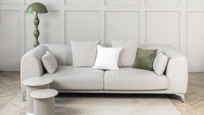 Stylish neutral living room scene featuring a soft beige sofa white cushions, a green floor lamp, and a textured light rug on warm wooden flooring. Demonstrating Pantone color of the year 2026 - Cloud Dancer