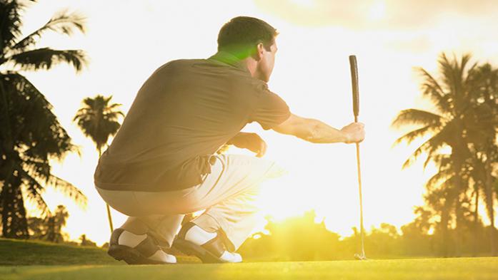 photo of golfer looking at putt with sunset behind him