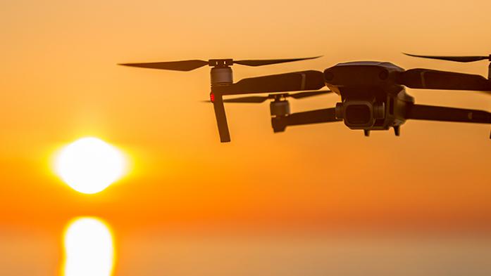 Image of drone flying over a sunset over the ocean