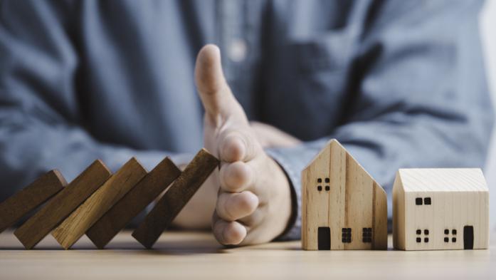 Businessman hand protect and stop wooden house from domino falling wooden bar for risk management and analysis of real estate concep
