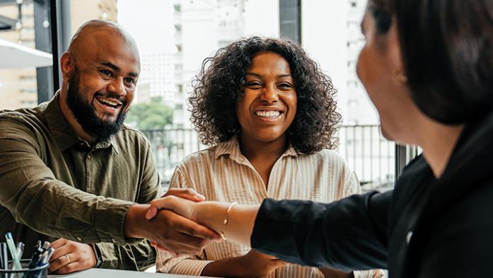 Photo of a real estate agent shaking hands with a couple clients in the office