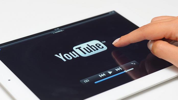 Photo of YouTube logo on an iPad with a hand pointing at it