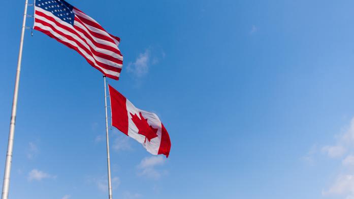 us flag and canadian flag against blue sky