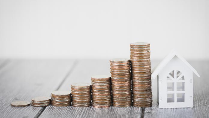 Small paper house with coins stacked up beside it