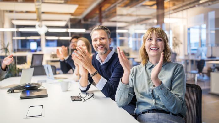 People at an office table clapping and smiling
