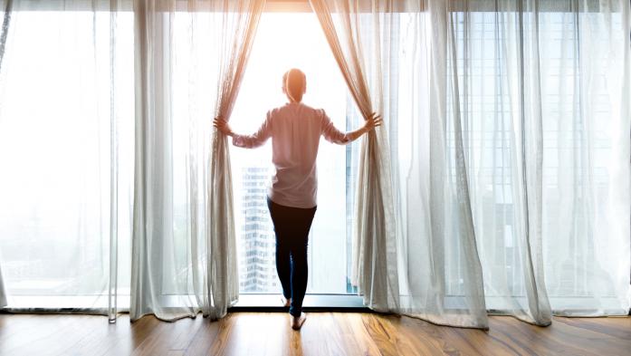 woman holding curtains open looking out window