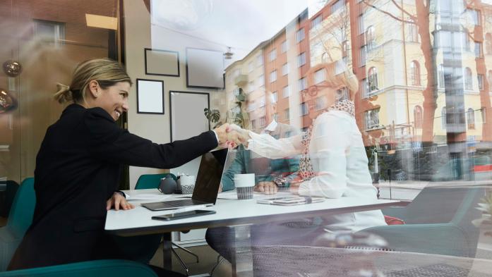 Woman shaking hands with image of another woman in the window