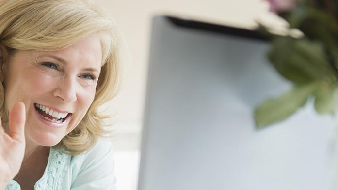 woman smiling and waving at computer screen