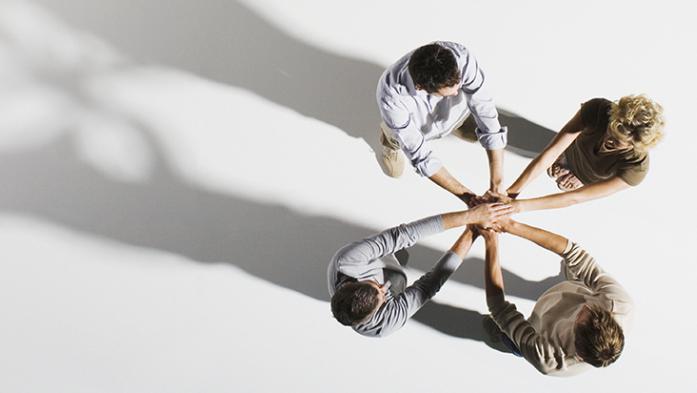 four people with hands on top of each others