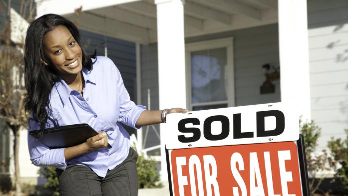 Woman smiling beside a for-sale sign with sold posted over it