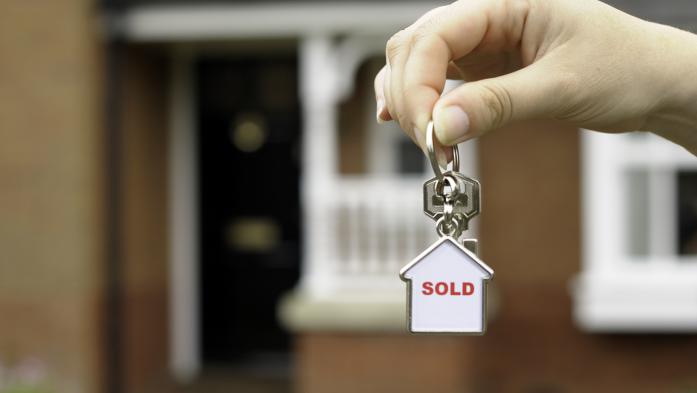 Hand in front of a house holding keychain with "sold" inside small house