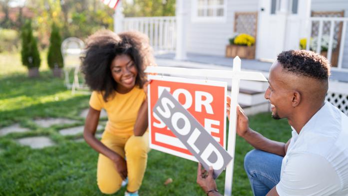 Husband and wife showing off sold sign in front of house