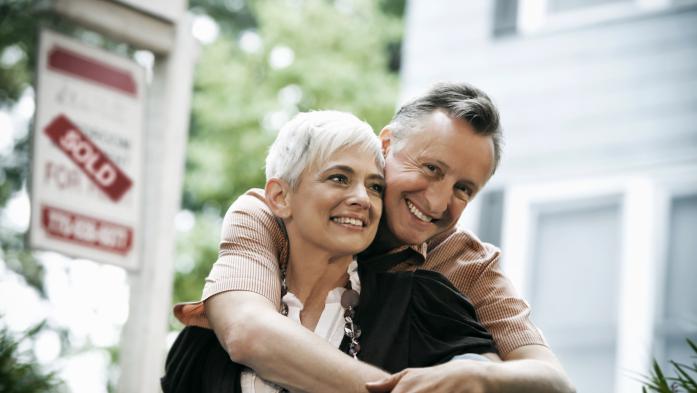 Couple in their sixties in front of a sign that they sold their home