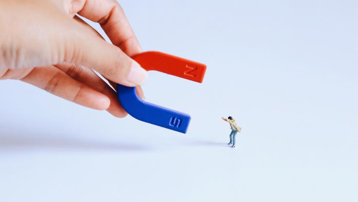Large hand with a magnet is pulling at tiny man