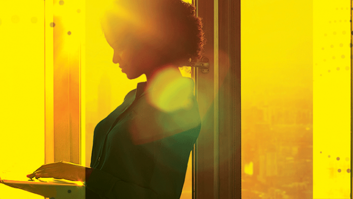 Photo of a woman standing looking at her laptop with a yellow color wash