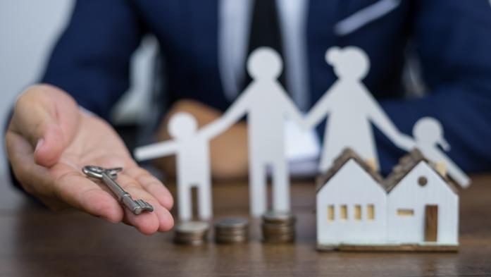 hand holding a key with family paper figures and small toy house in background