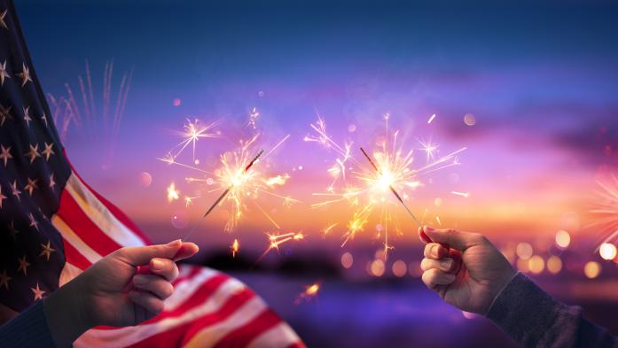 July 4 celebration hands holding sparklers with flag behind on left
