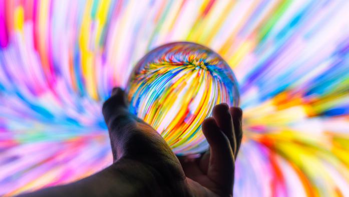 hand holding crystal ball with rainbow swirls all around it