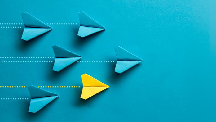 photo illustration of paper air planes flying in one direction over blue background