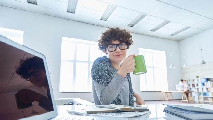 woman at computer desk holding coffee cup